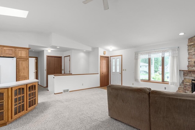 living room featuring lofted ceiling, light colored carpet, ceiling fan, and a stone fireplace