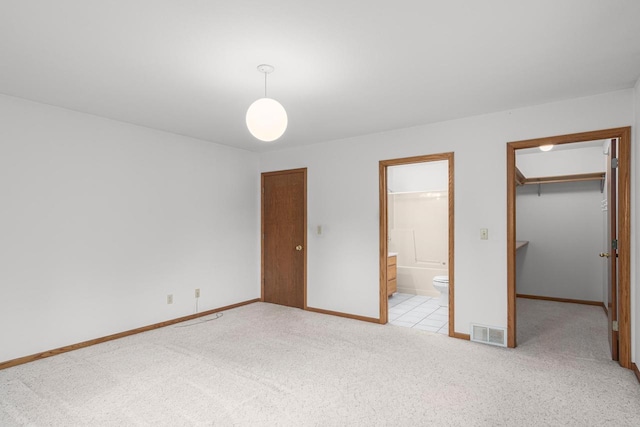 unfurnished bedroom featuring a closet, light colored carpet, a spacious closet, and ensuite bathroom