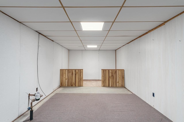 basement featuring light colored carpet, wood walls, and a paneled ceiling