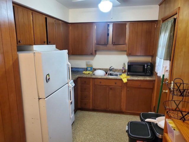 kitchen featuring brown cabinetry, freestanding refrigerator, range, and a sink