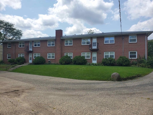 multi unit property with a chimney, a front lawn, and brick siding