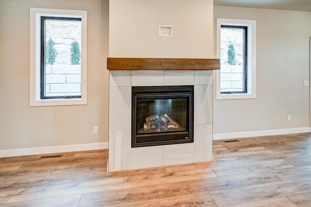 room details featuring visible vents, a fireplace, baseboards, and wood finished floors