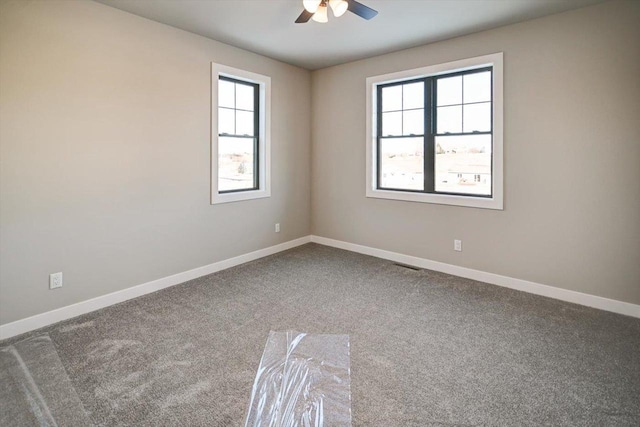 carpeted empty room featuring visible vents, a ceiling fan, and baseboards