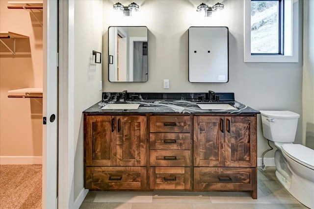 bathroom with double vanity, baseboards, toilet, a spacious closet, and a sink