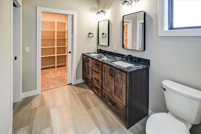 bathroom with toilet, double vanity, baseboards, and a sink