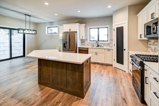 kitchen featuring light wood finished floors, white cabinets, stainless steel appliances, light countertops, and a sink