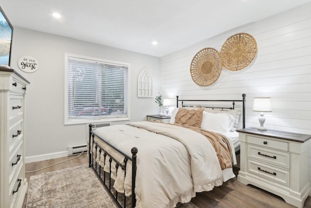 bedroom featuring a baseboard heating unit, wood-type flooring, and wood walls