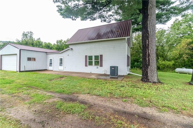 rear view of house featuring a lawn, a garage, an outbuilding, and central AC unit