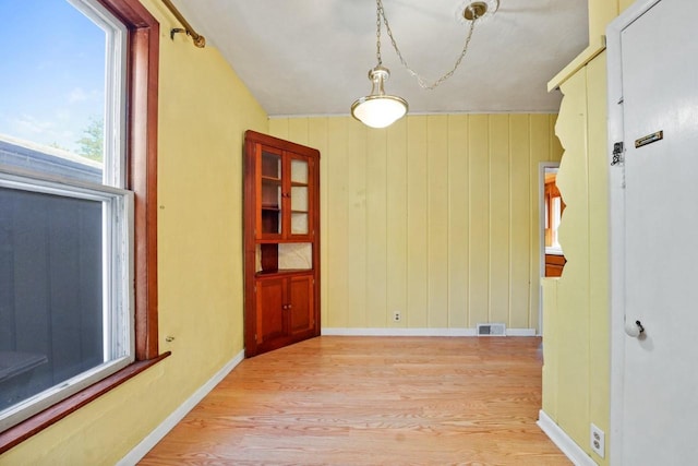 unfurnished dining area featuring lofted ceiling, wooden walls, and light hardwood / wood-style flooring