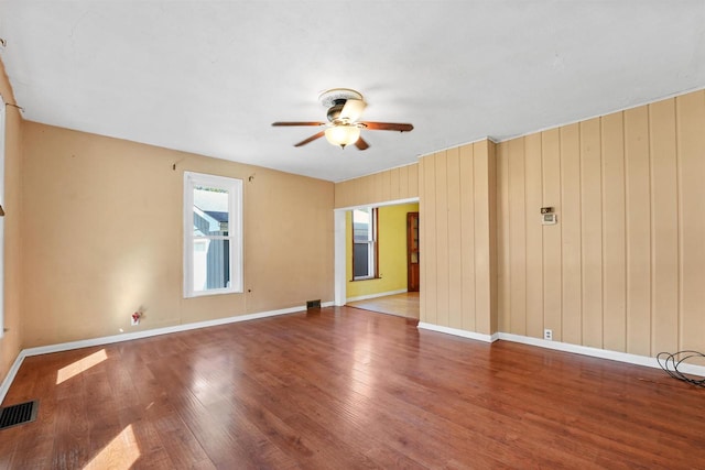 empty room featuring hardwood / wood-style floors, ceiling fan, and wood walls