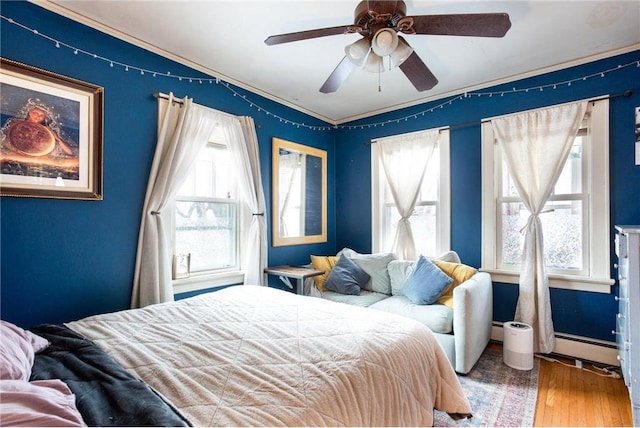 bedroom with baseboard heating, ceiling fan, wood-type flooring, and multiple windows