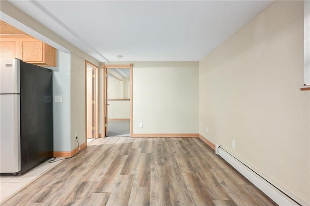 interior space featuring a baseboard heating unit, light brown cabinetry, stainless steel fridge, and light wood-type flooring