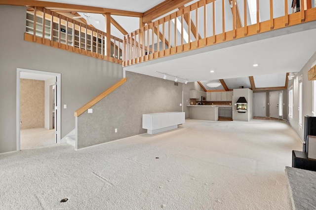 unfurnished living room with carpet floors, beam ceiling, high vaulted ceiling, ceiling fan, and track lighting