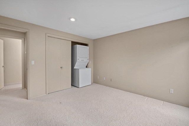 unfurnished bedroom featuring stacked washer and clothes dryer and light carpet