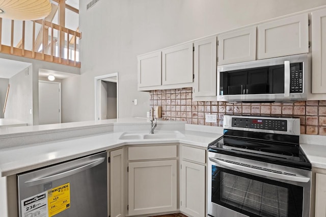 kitchen featuring stainless steel appliances, tasteful backsplash, white cabinets, and a high ceiling