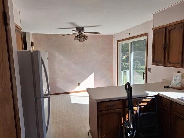 kitchen featuring light colored carpet, ceiling fan, white fridge, and kitchen peninsula