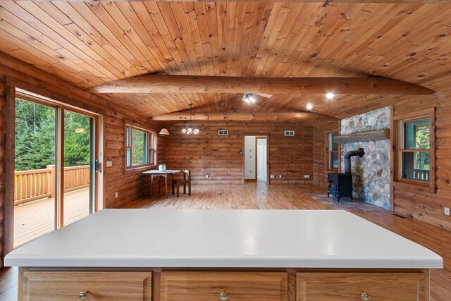 kitchen featuring wood walls, vaulted ceiling with beams, wood ceiling, a wood stove, and light hardwood / wood-style flooring