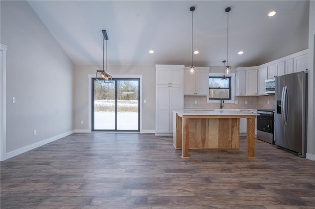 kitchen featuring a kitchen island, vaulted ceiling, decorative light fixtures, stainless steel appliances, and white cabinets