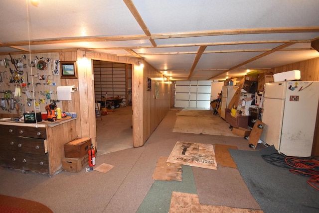 garage with a workshop area, white refrigerator, and wood walls