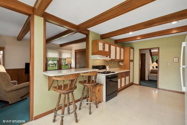 kitchen featuring gas range, light countertops, under cabinet range hood, a kitchen bar, and beam ceiling