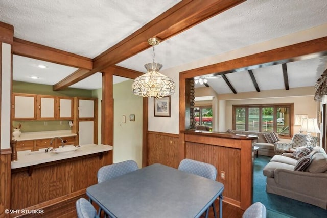 dining area with dark wood-type flooring, beam ceiling, wainscoting, and a textured ceiling