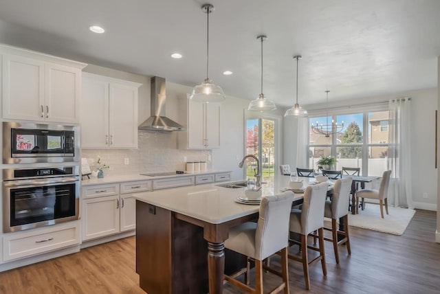 kitchen with a sink, wall chimney range hood, stainless steel appliances, light countertops, and decorative backsplash