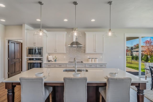 kitchen featuring a sink, wall chimney range hood, appliances with stainless steel finishes, light countertops, and decorative backsplash