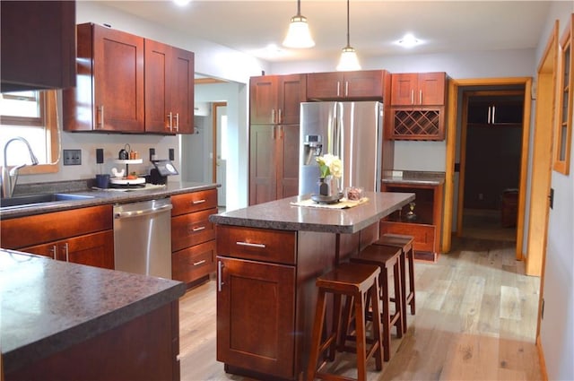 kitchen featuring decorative light fixtures, light hardwood / wood-style flooring, appliances with stainless steel finishes, a center island, and sink