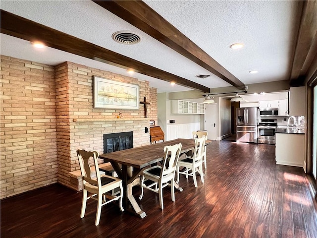 dining area with beamed ceiling, a textured ceiling, a brick fireplace, sink, and dark hardwood / wood-style floors