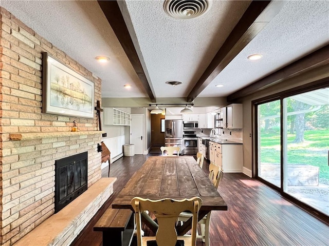 interior space with a textured ceiling, beamed ceiling, appliances with stainless steel finishes, dark wood-type flooring, and a brick fireplace