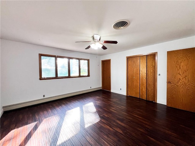 unfurnished bedroom with dark wood-type flooring, ceiling fan, a baseboard radiator, and multiple closets