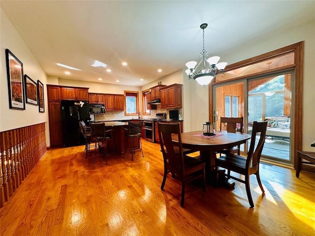 dining room with recessed lighting, light wood-style flooring, an inviting chandelier, and a wainscoted wall