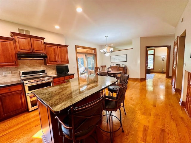 kitchen with double oven range, a breakfast bar, light wood-style flooring, under cabinet range hood, and backsplash