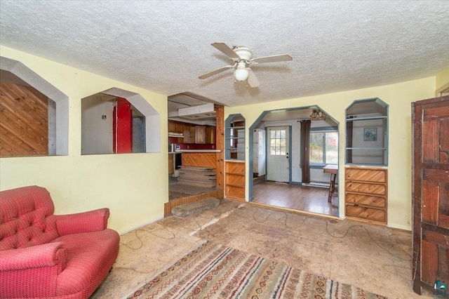 living room with a textured ceiling, ceiling fan, and wood-type flooring