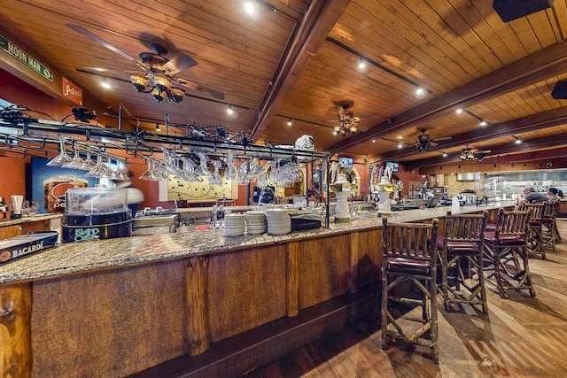 bar with a ceiling fan, wooden ceiling, wood finished floors, wet bar, and beam ceiling