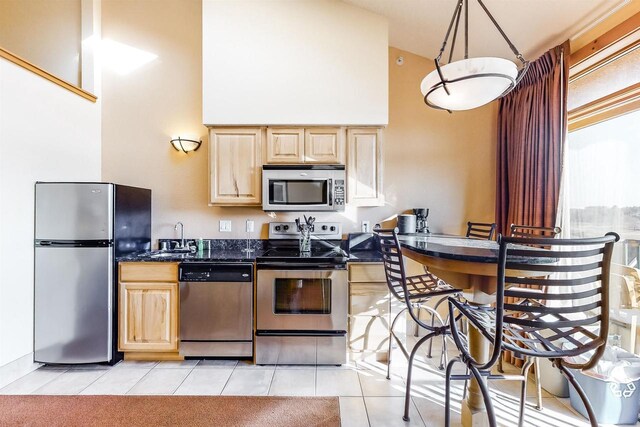 kitchen featuring light tile patterned floors, appliances with stainless steel finishes, sink, light brown cabinets, and high vaulted ceiling