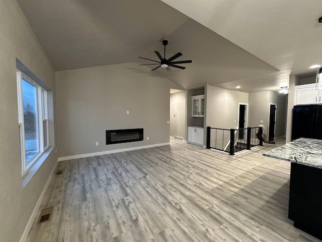 unfurnished living room with a glass covered fireplace, visible vents, light wood-style flooring, and baseboards