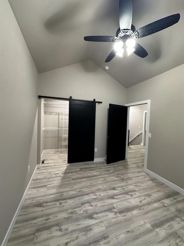 unfurnished bedroom with light wood finished floors, a barn door, baseboards, a ceiling fan, and lofted ceiling