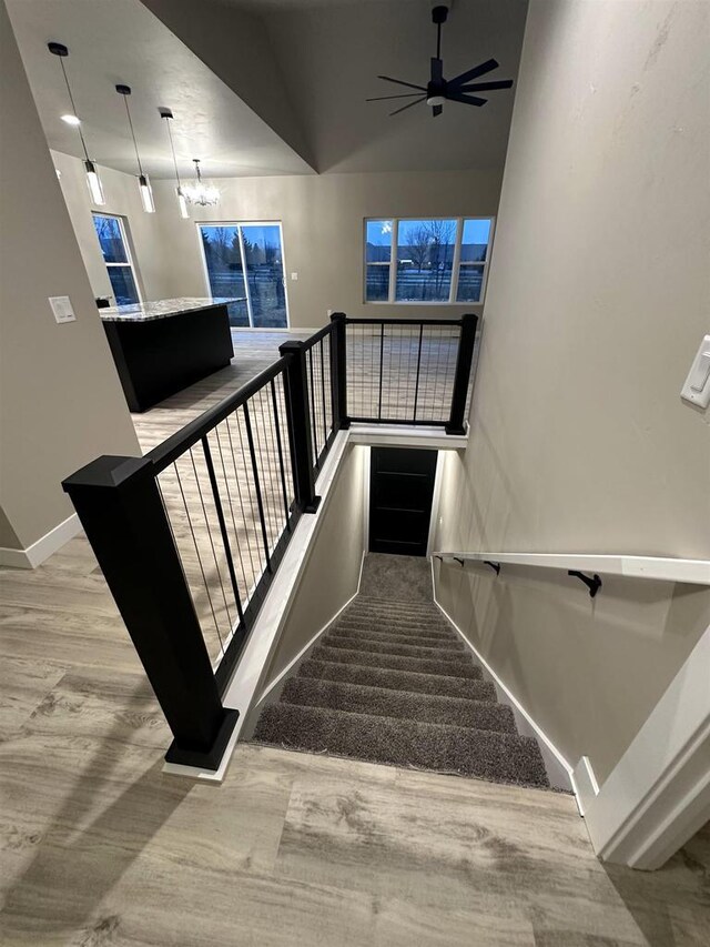 staircase featuring ceiling fan with notable chandelier, wood finished floors, and baseboards