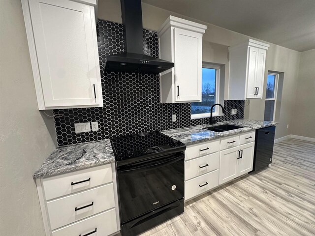 kitchen featuring backsplash, white cabinets, a sink, black appliances, and wall chimney exhaust hood