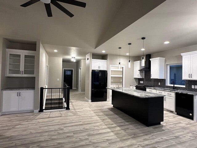 kitchen featuring light wood finished floors, tasteful backsplash, wall chimney exhaust hood, a kitchen island, and black appliances