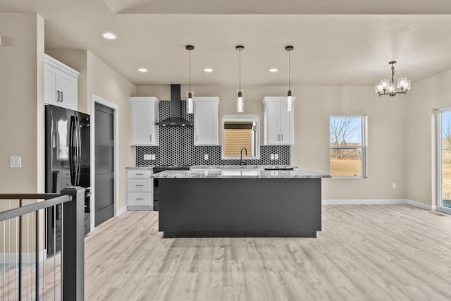 kitchen featuring wall chimney range hood, light wood-style floors, freestanding refrigerator, and a center island