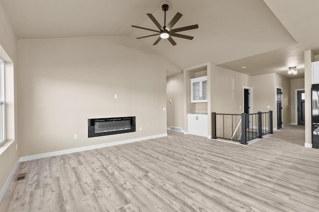 unfurnished living room with light wood-style flooring, visible vents, baseboards, and a glass covered fireplace