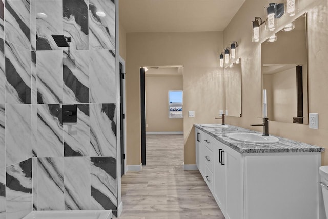 bathroom with wood finished floors, double vanity, a sink, and walk in shower