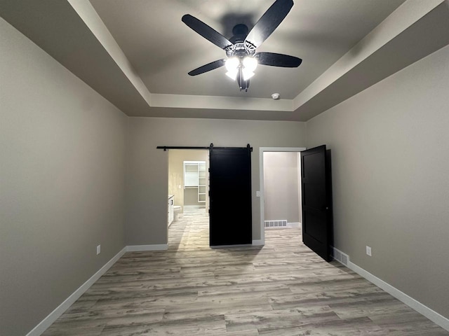 unfurnished bedroom with a barn door, wood finished floors, visible vents, baseboards, and a tray ceiling