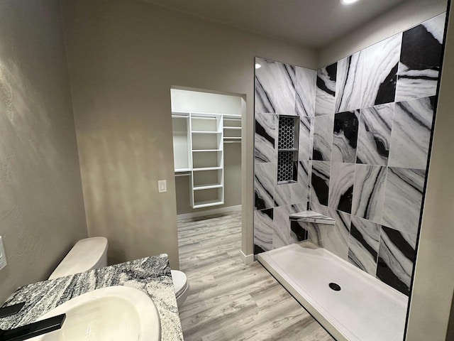 full bath with a sink, a tile shower, toilet, and wood finished floors