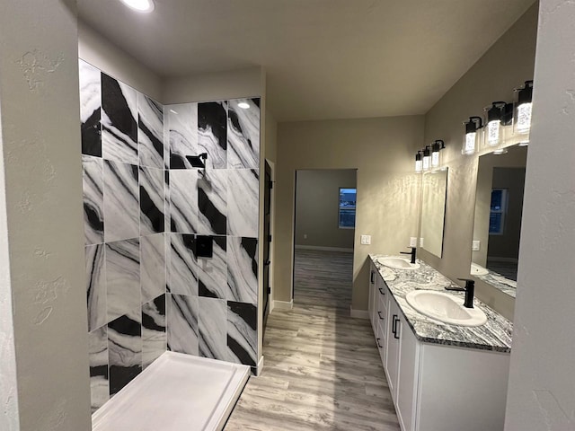 bathroom featuring wood finished floors, double vanity, tiled shower, and a sink