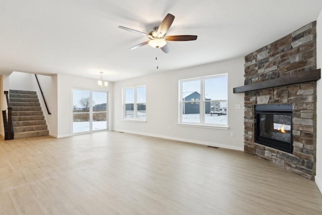 unfurnished living room with a fireplace, ceiling fan with notable chandelier, and light hardwood / wood-style floors