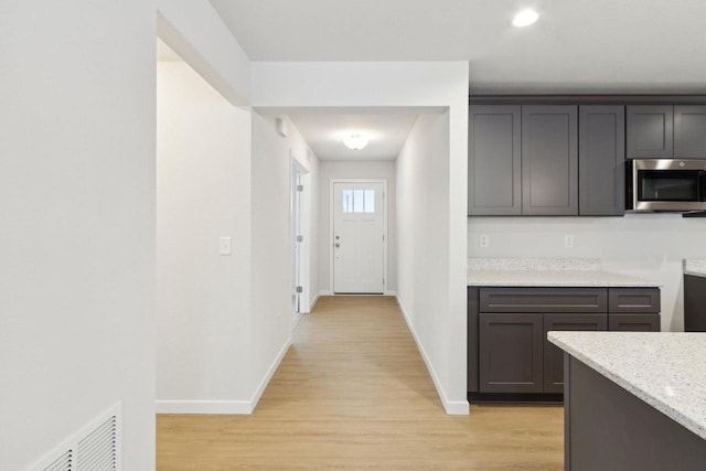 kitchen featuring dark brown cabinetry, light stone countertops, and light wood-type flooring