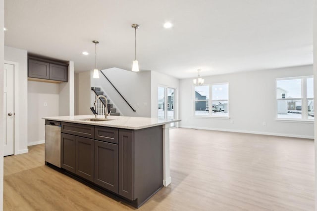 kitchen featuring sink, light stone counters, stainless steel dishwasher, decorative light fixtures, and light wood-type flooring